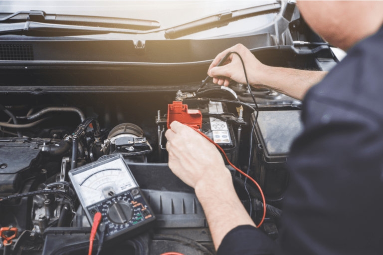 Mobile dash cam installation technician using a multi-meter to test car battery voltage.